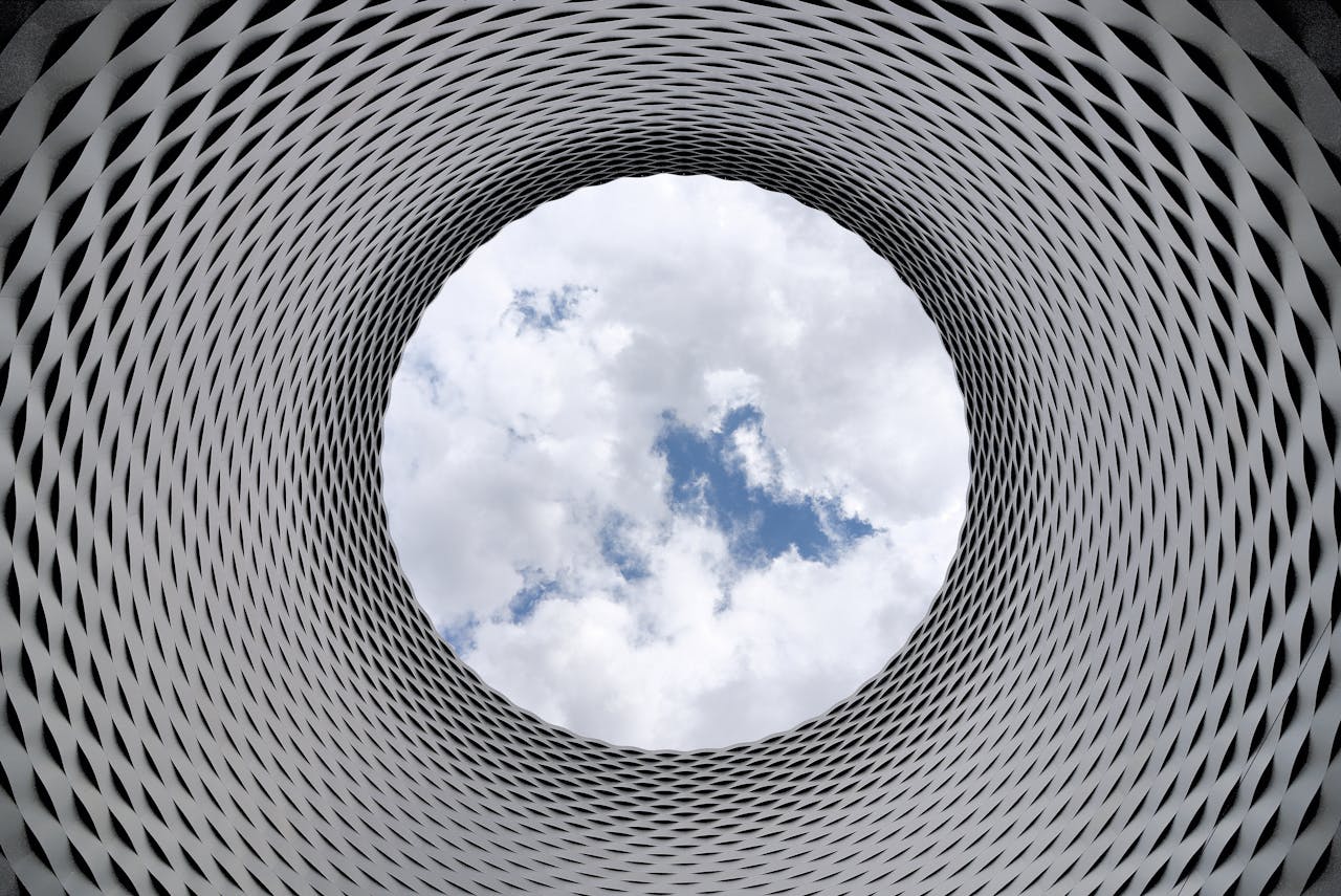 about-us-02 Modern architectural tunnel with a geometric pattern revealing a bright sky.